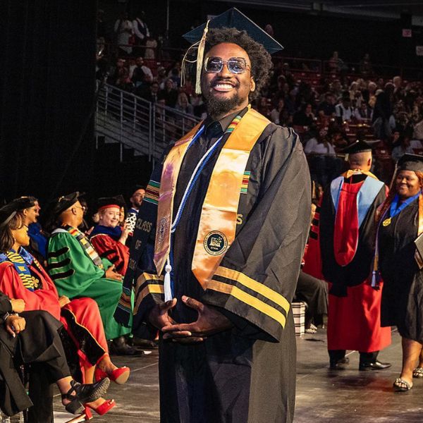 A student in a cap and gown smiles at a Community College of Philadelphia commencement ceremony