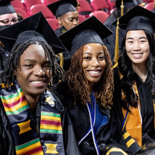 Three students smile while seated at a Community College of Philadelphia commencement ceremony.