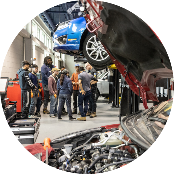 A group of students learn automotive mechanics in a garage full of cars