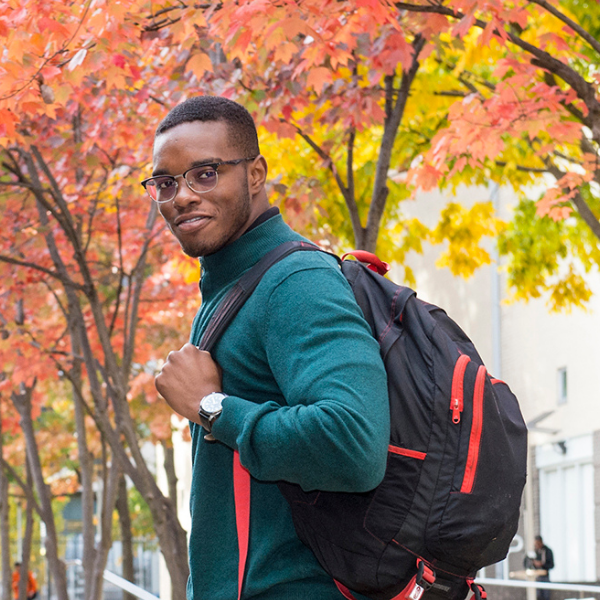 A student with a backpack walks through a courtyard in Autumn with trees of red, gold, and green leaves fill the background